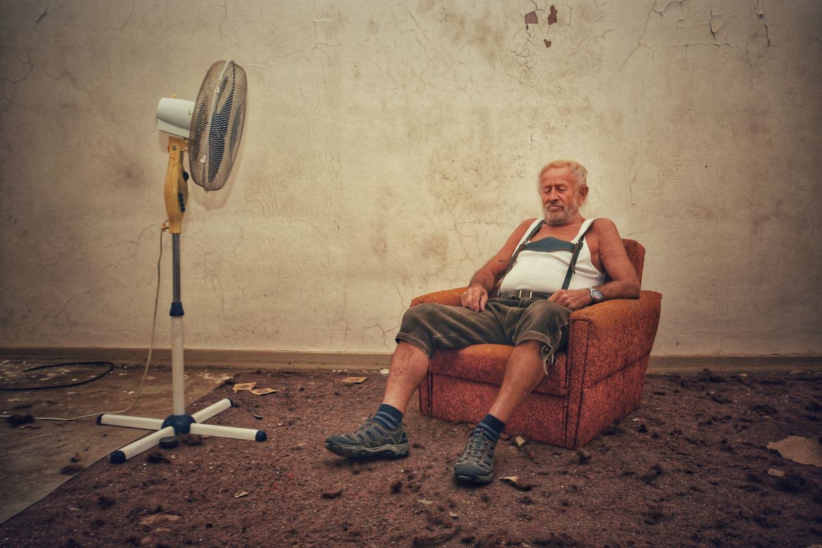 An elderly man cooling off in front of a fan