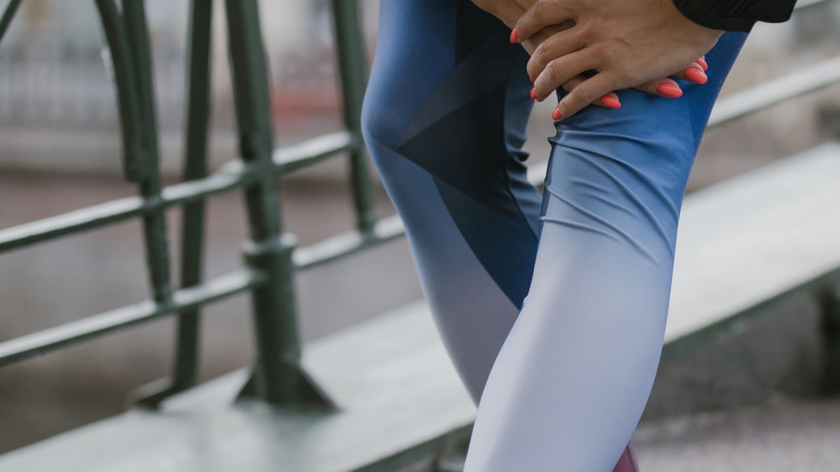 A person in athletic clothing holding a sore leg outdoors after exercise