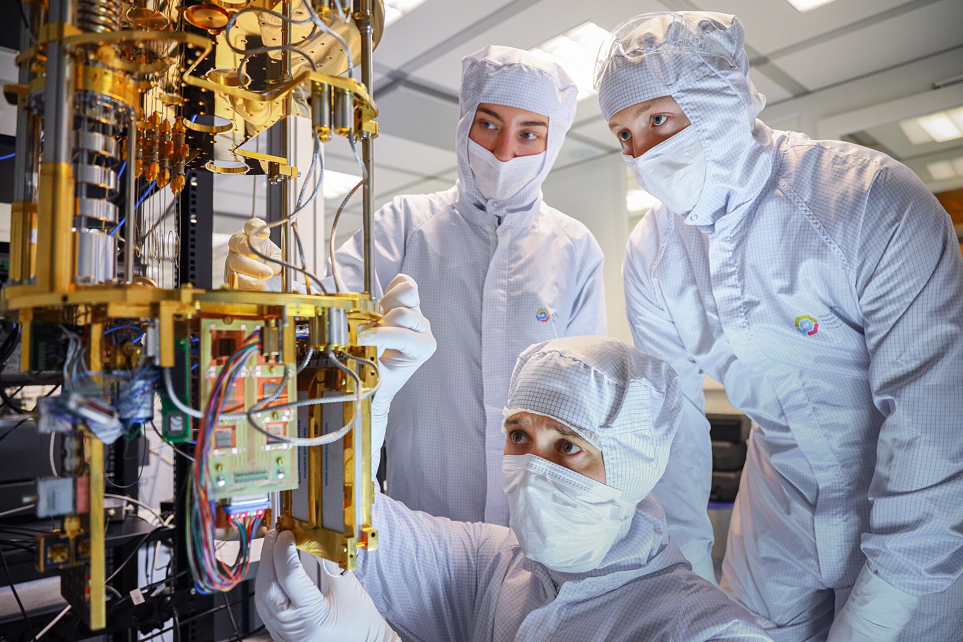 Researchers in cleanroom suits working on a gold-plated dilution refrigerator holding a superconducting quantum processor